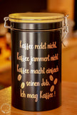 Schwarze Kaffeedose mit Bambusdeckel und Bügelverschluss in Kaffeebar, auf Holztresen. Mit Spuch Kaffee redet nicht.