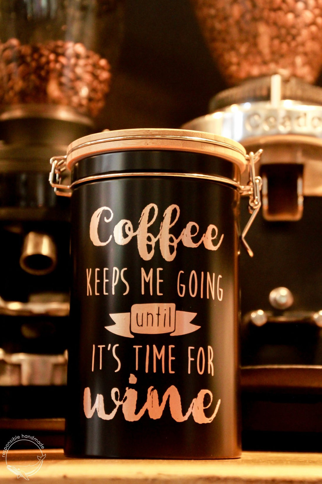 Schwarze Kaffeedose mit Bambusdeckel und Bügelverschluss in Kaffeebar, rosegoldener Spruch: Coffee KEEPS ME GOING