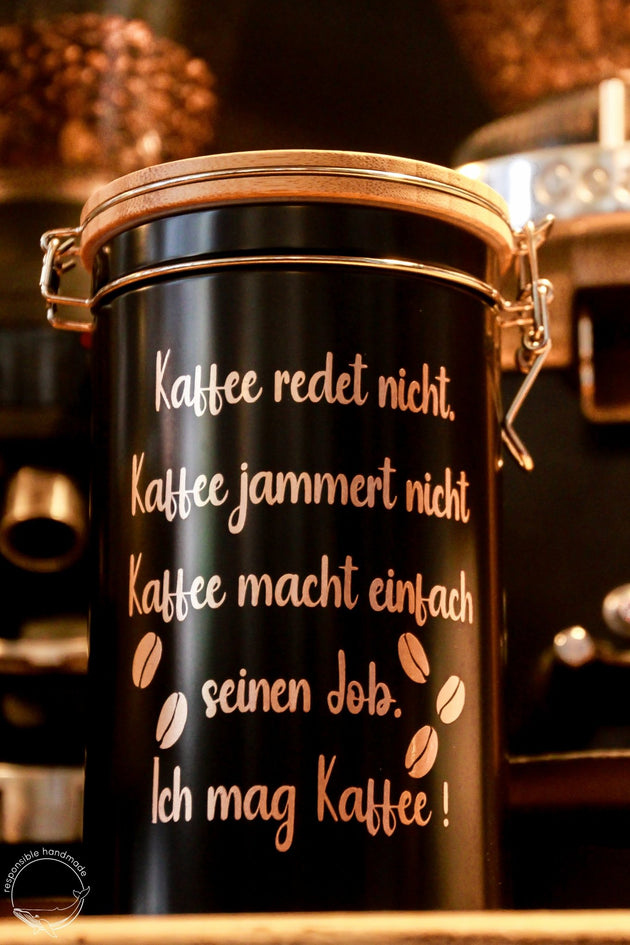 Schwarze Kaffeedose mit Bambusdeckel und Bügelverschluss in Kaffeebar, rosegoldener Spruch: Kaffee redet nicht.
