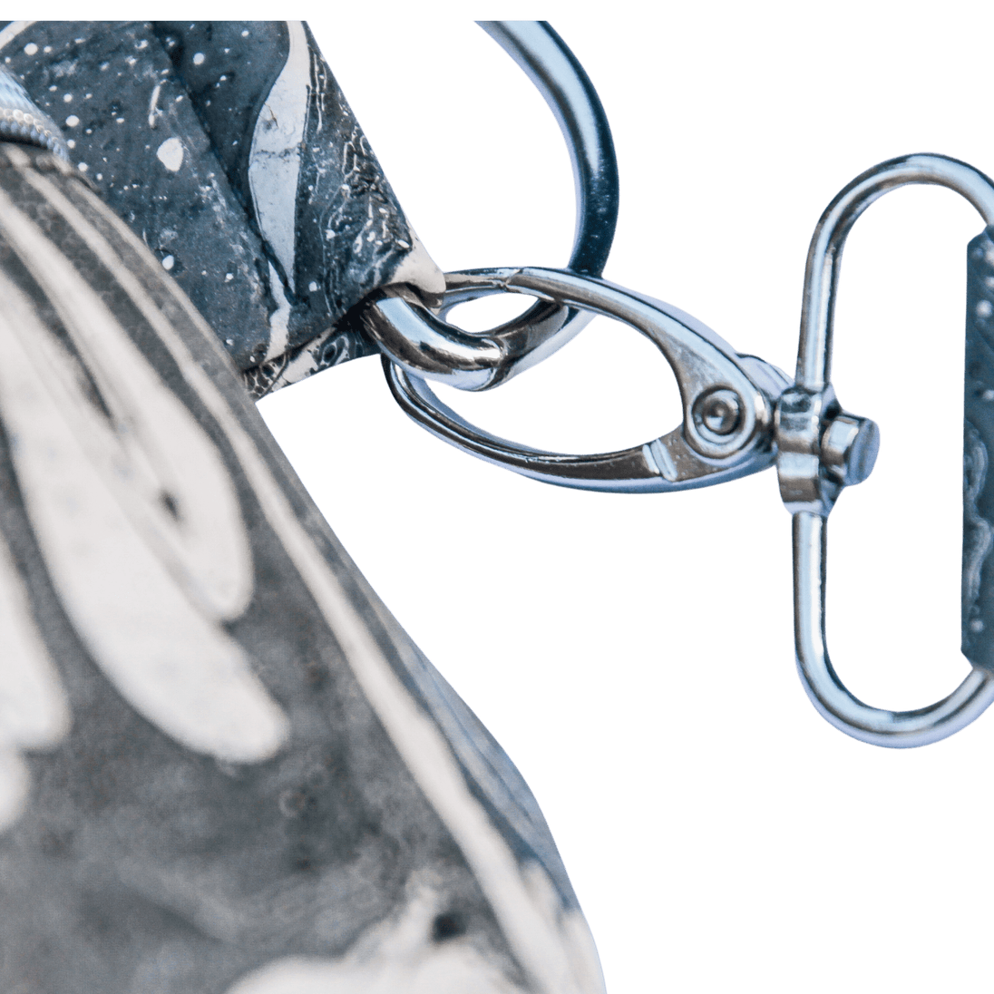 Detailbild der Grurtbandaufhängung an einem silbernen D-Ring und Karabiner der Slingbag aus handmarmoriertem Kork, Farbe schwarz und weiß 