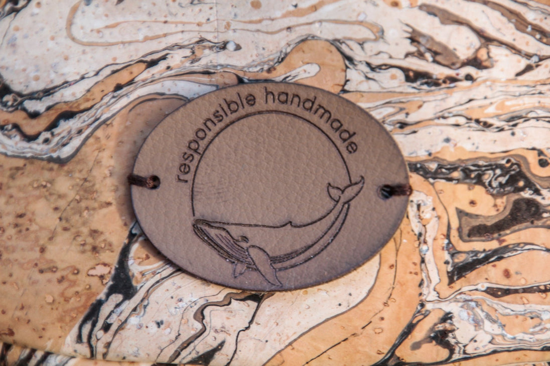 Detailbild des Labels aus Kaktusleder auf dem ein Wal und "responsible handmade" zu sehen sind auf der Slingbag in braun/weiß marmoriertem Kork